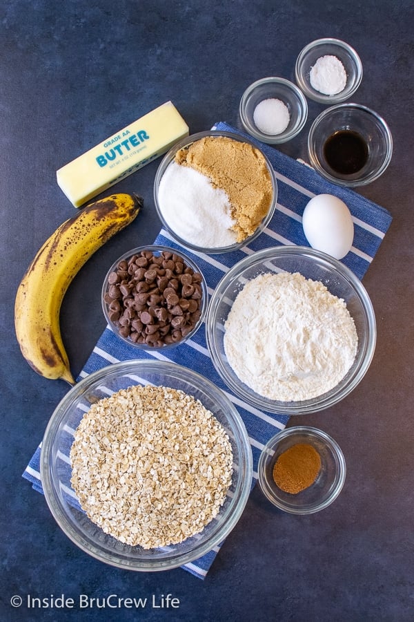 A blue board with bowls of ingredients to make oatmeal chocolate chip banana cookies on it