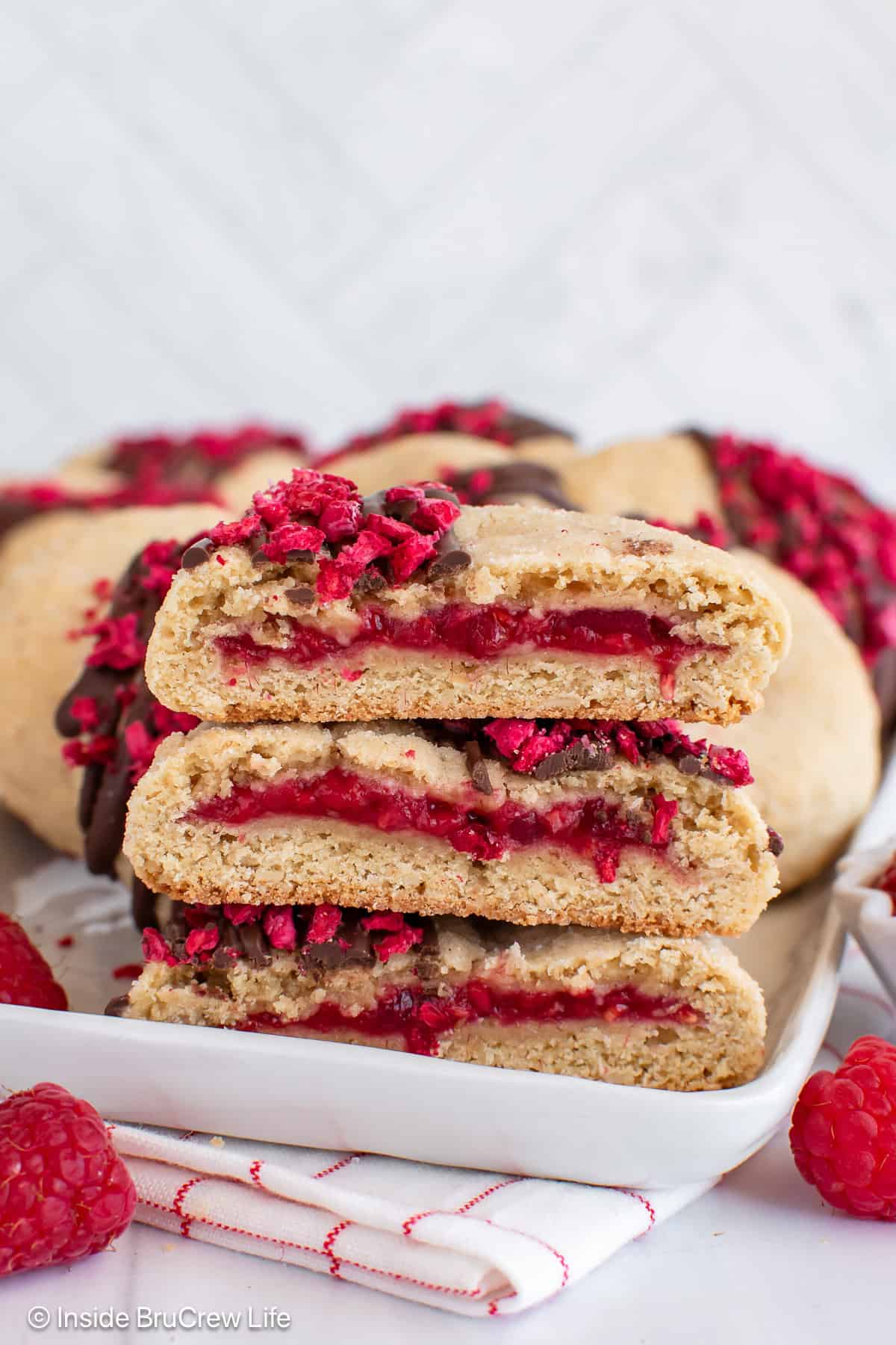 A tray of raspberry filled cookies with three cookie halves showing the fruit center.