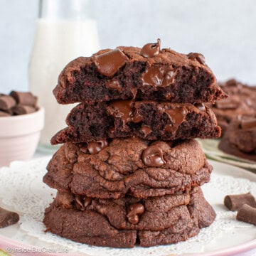 A stack of double chocolate chunk cookies on a white plate with the top cookie broken in half showing the gooey center.