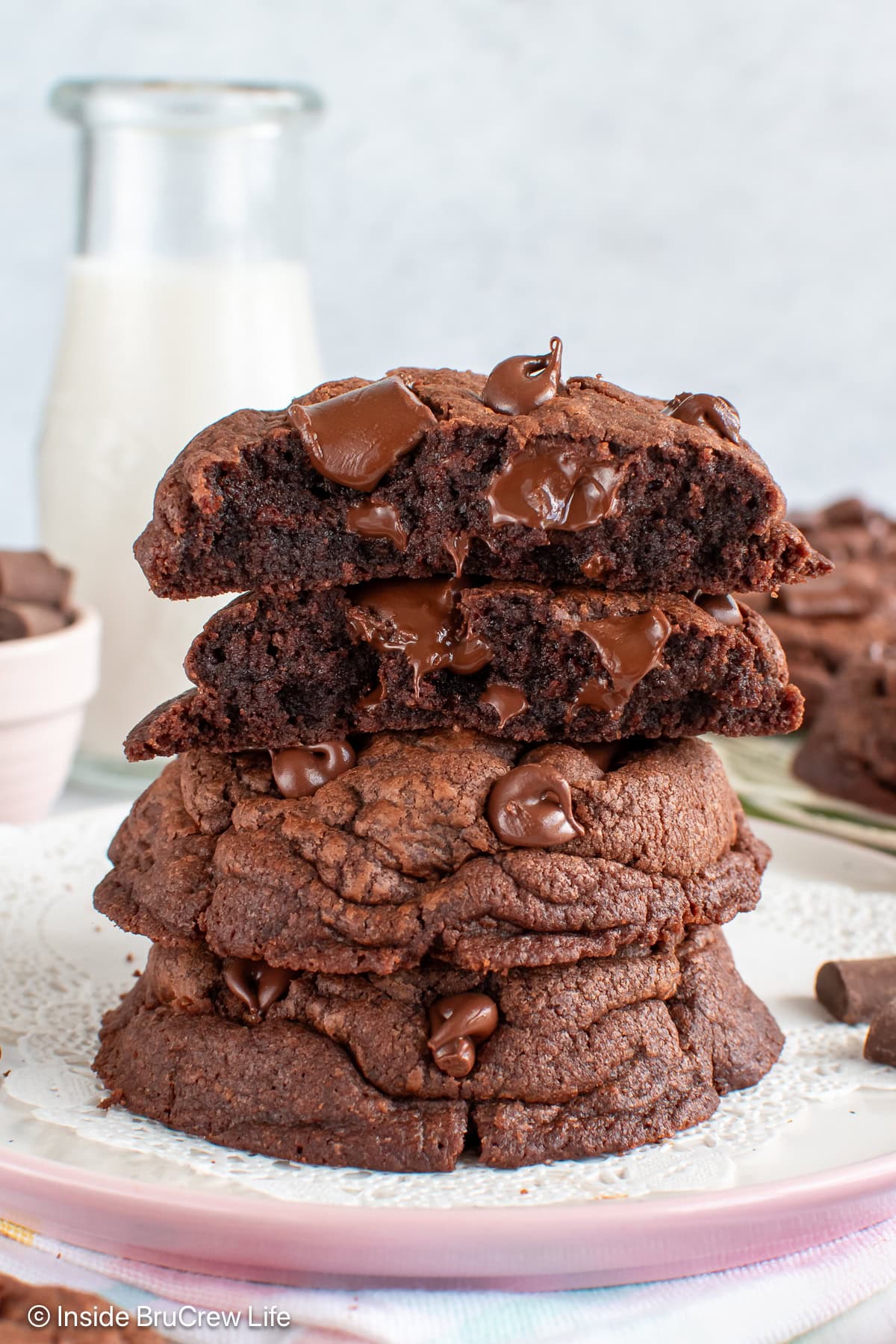 A stack of double chocolate chunk cookies on a white plate with the top cookie broken in half showing the gooey center.