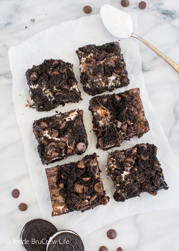 Brownies topped with marshmallow and Oreo cookie crumbs lined up on a white board.