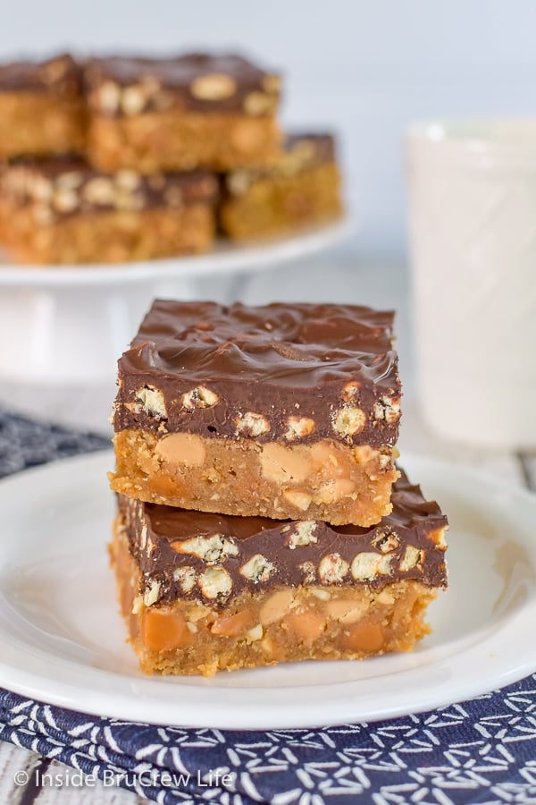 A white plate on a blue towel with two homemade take 5 bars stacked on it and a plate of bars behind it