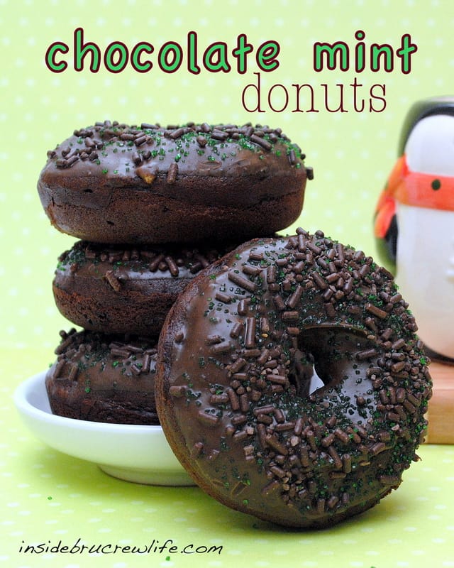 3 chocolate donuts stacked with one standing in front all on a green and white polka dot background.