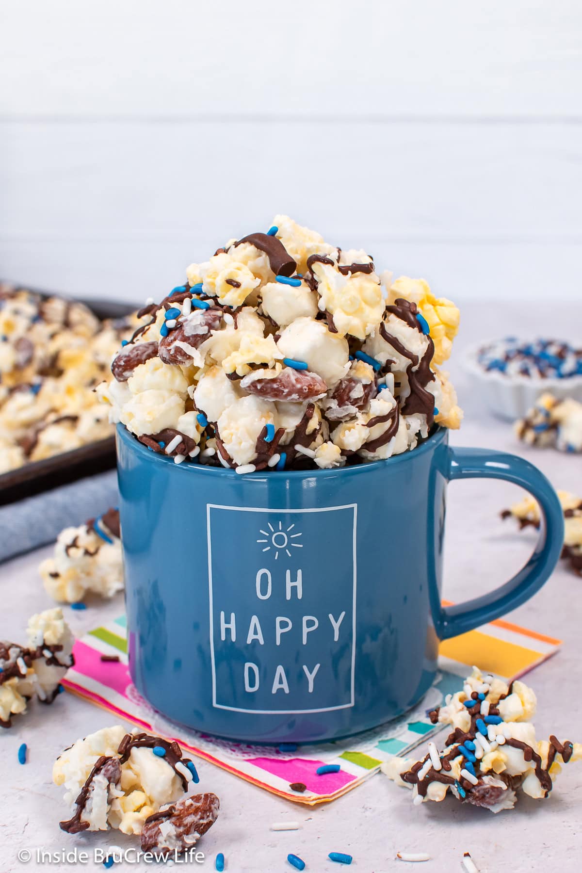 A blue cup filled with a chocolate drizzled coconut popcorn.
