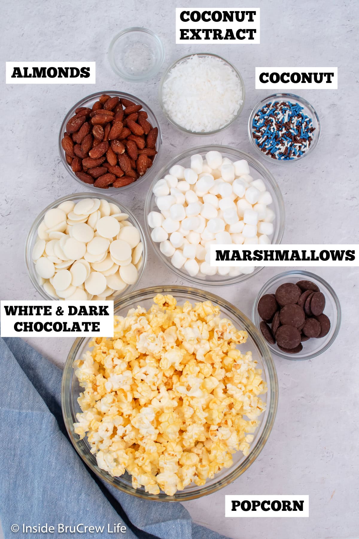 A white board with bowls of ingredients needed to make chocolate coconut popcorn.