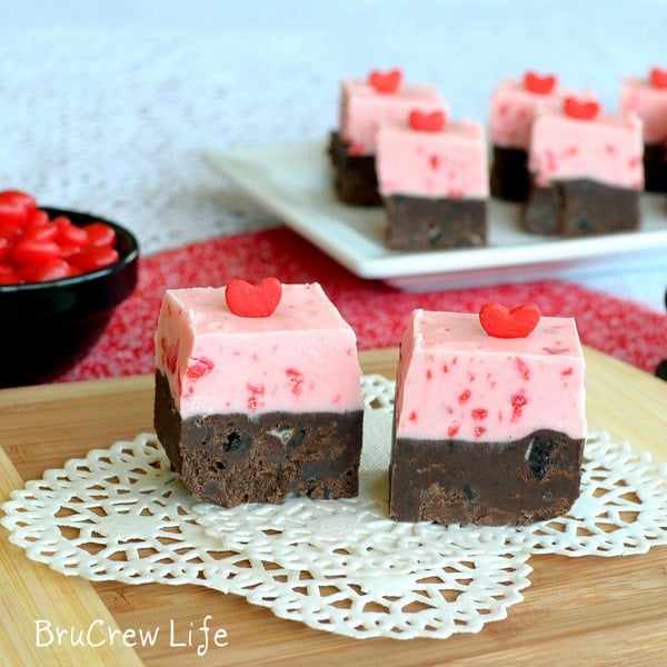 A white doily with two squares of Red Hot Oreo Fudge with heart sprinkles on top showing the two layers of fudge in each one