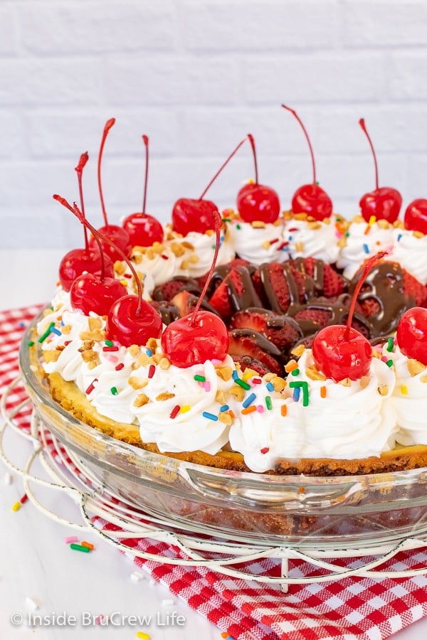 A pie topped with cool whip swirls, cherries, and sprinkles on a red and white towel.