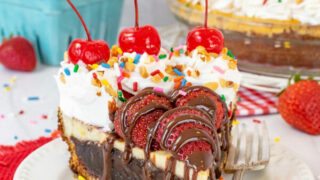 A white plate with a slice of banana split brownie pie topped with strawberries, cool whip, cherries, and sprinkles.