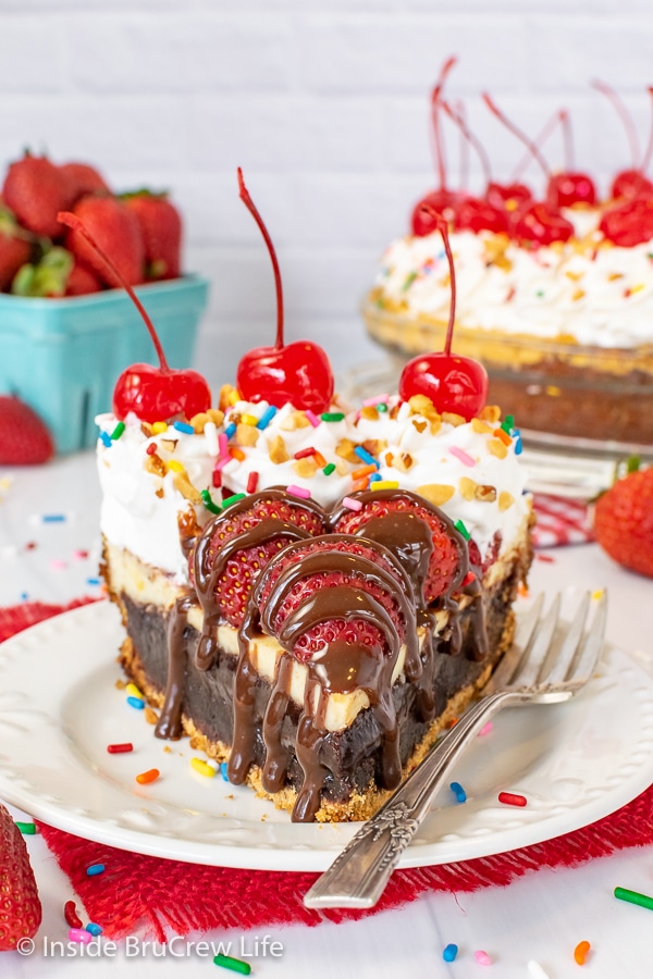A slice of banana split brownie pie with lots of toppings on a white plate with a fork