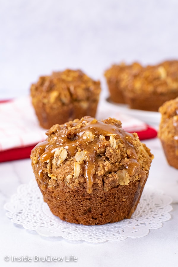 A Biscoff Apple Muffin with a drizzle of cookie butter glaze on top sitting on a white doily