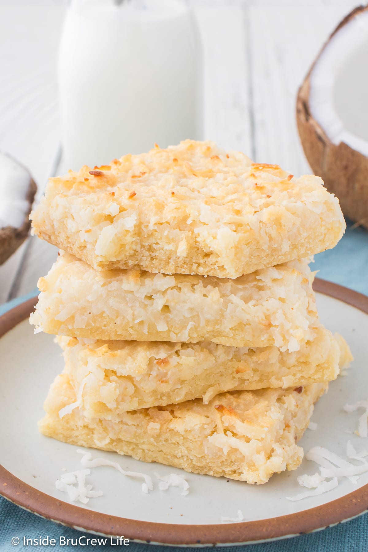 A stack of four gooey bars made with coconut on a plate.