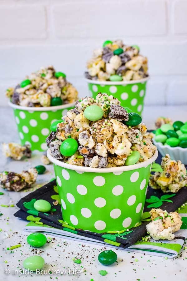 A green bowl with white polka dots filled with chocolate popcorn and green M&M's.