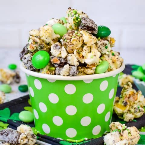 A green bowl with white polka dots filled with chocolate popcorn and green M&M's.