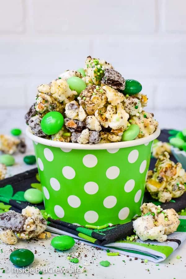 A green bowl with white polka dots filled with chocolate popcorn and green M&M's.