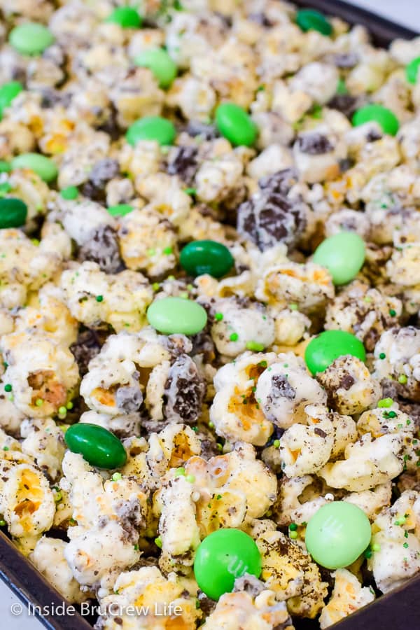 A tray of white chocolate covered popcorn with mint cookies and green M&M's.