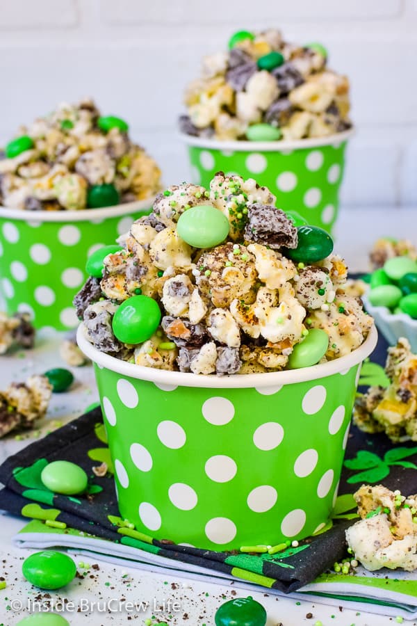 A green bowl with white polka dots filled with chocolate popcorn and green M&M's.