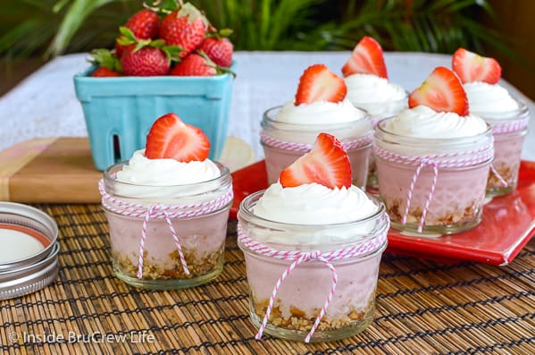 Six glass jars filled with no bake strawberry cheesecake and topped with Cool Whip and strawberries
