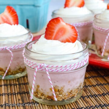 A glass jar filled with no bake strawberry cheesecake topped with Cool Whip and a strawberry