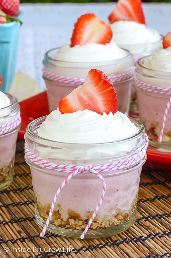 Close up picture of a glass jar filled with no bake strawberry cheesecake topped with Cool Whip and a strawberry