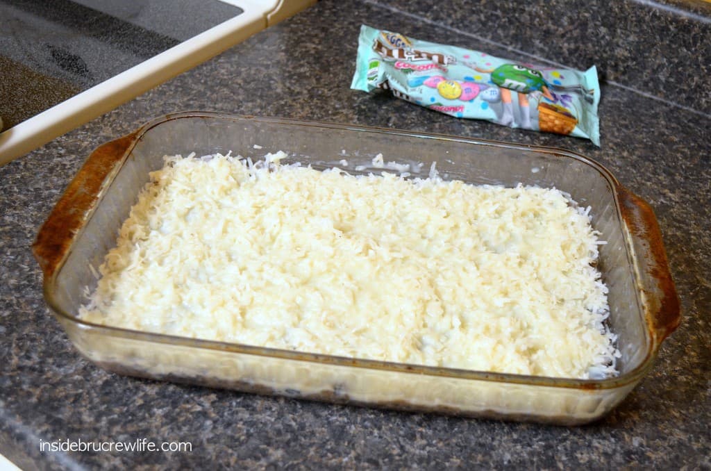 Cake bars topped with coconut in a clear 9x13 pan.