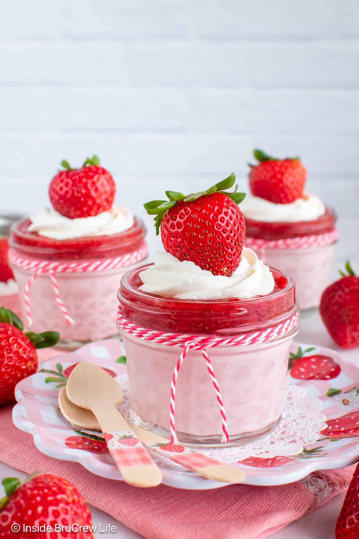Three strawberry cheesecake cups topped with strawberry chia jam and whipped cream.