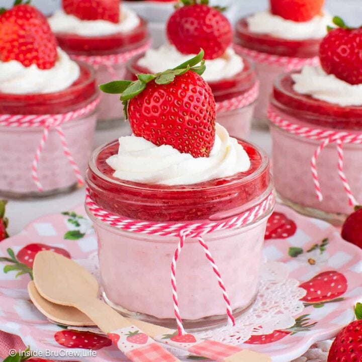 Six clear jars filled with no bake strawberry cheesecake and strawberry chia jam.