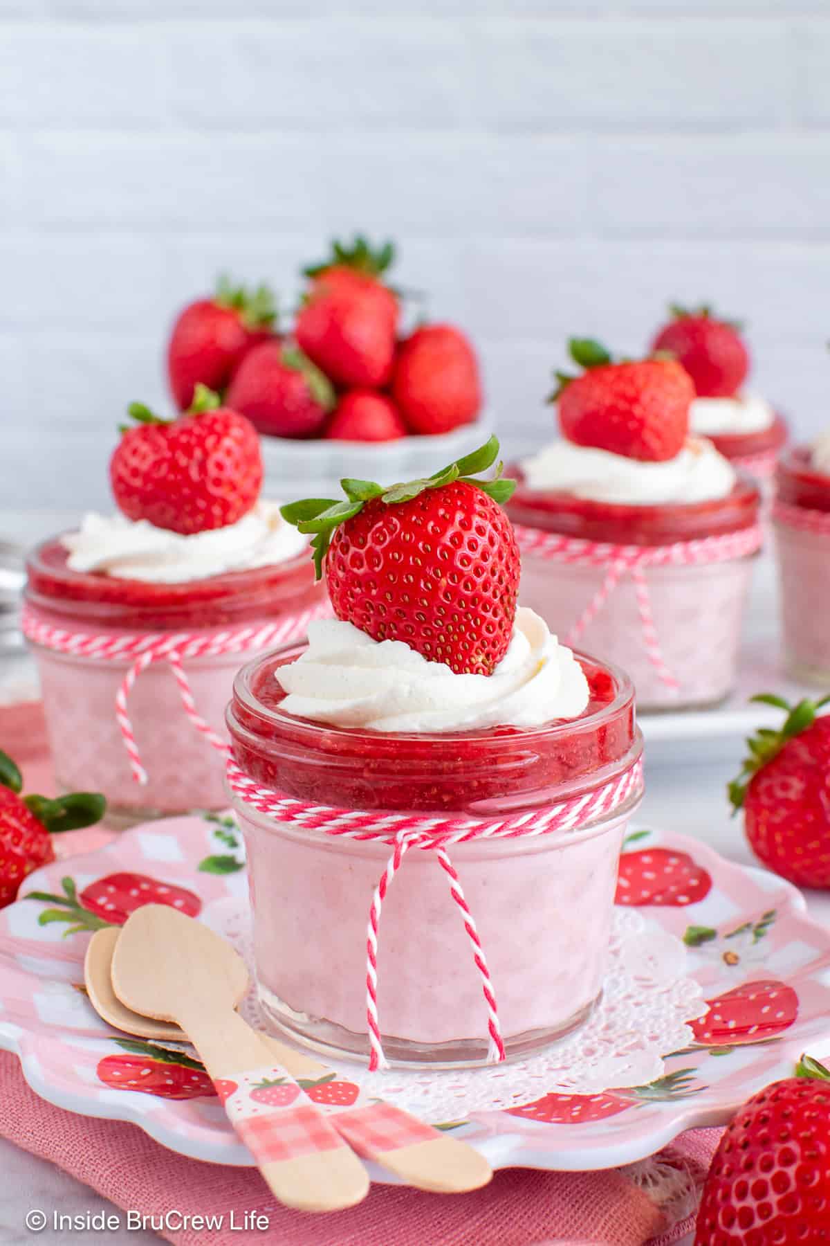 Four clear jars filled with no bake strawberry cheesecake and strawberry chia jam.