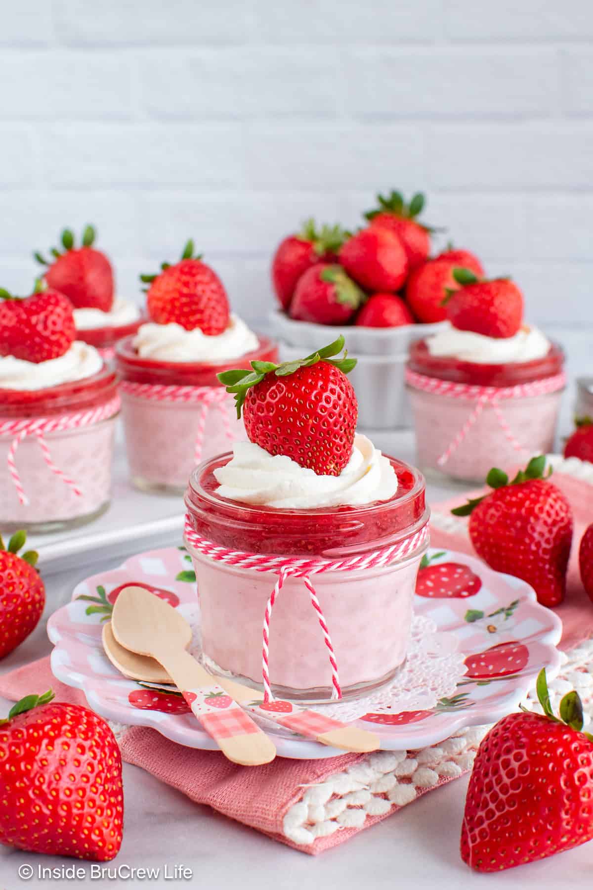 5 Strawberry cheesecake cups made with cottage cheese and topped with chia jam with strawberries behind it.