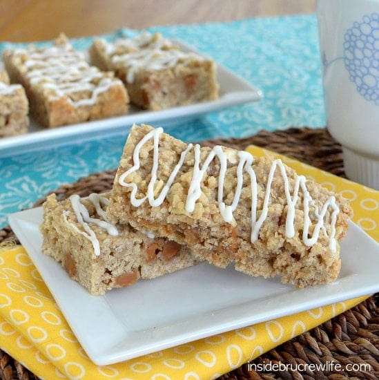 Two caramel oatmeal bars stacked on a white plate with more bars behind them