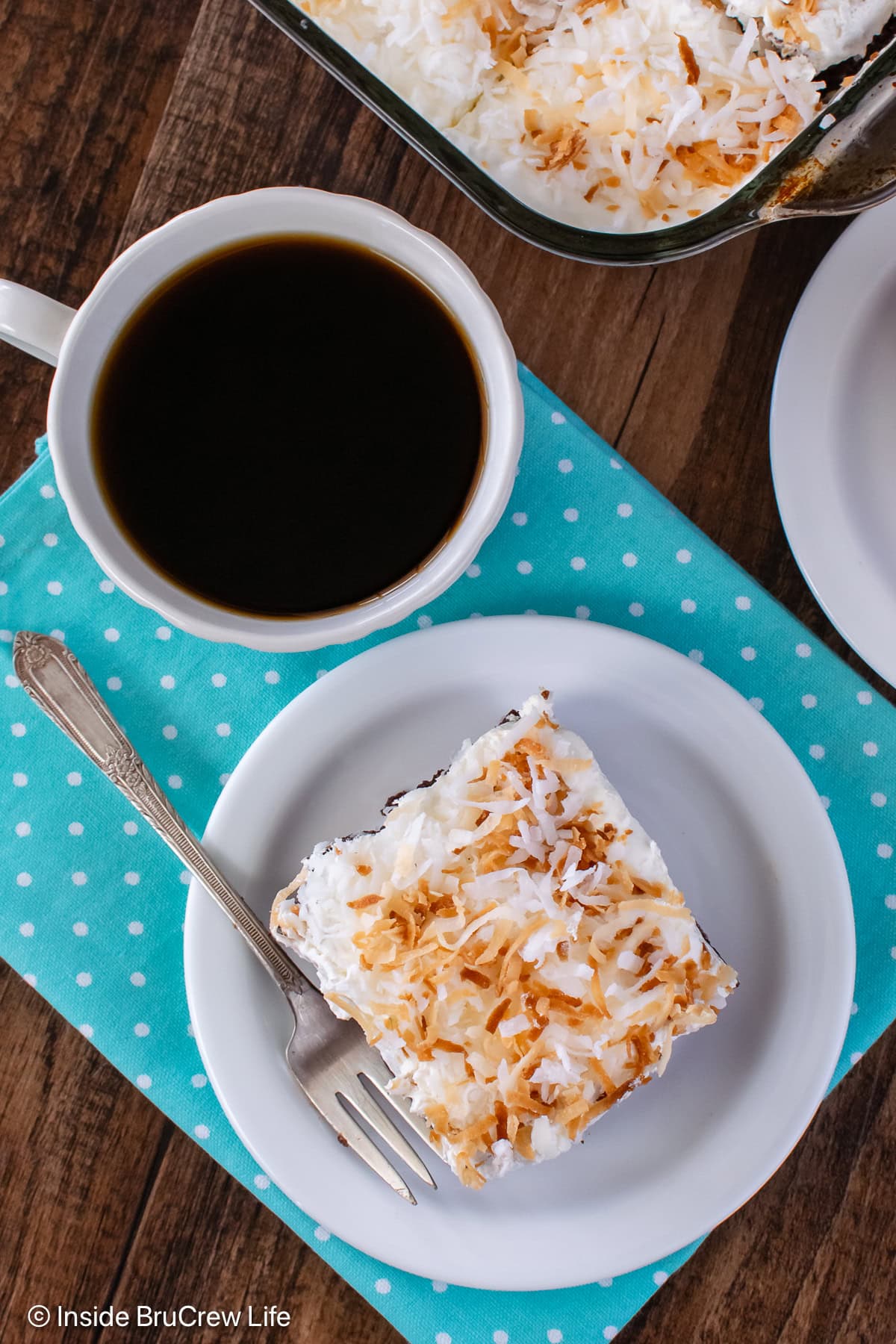 A slice of cake on a plate topped with Cool Whip and toasted coconut.