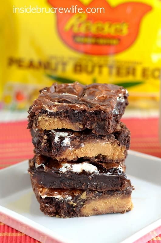 A stack of four Marshmallow Reese's Brownies on a white plate with a yellow bag of peanut butter eggs behind them.