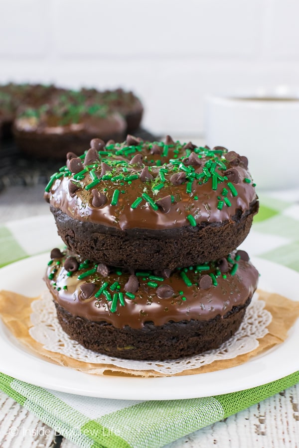 Two chocolate zucchini donuts topped with chocolate glaze stacked on a white plate.