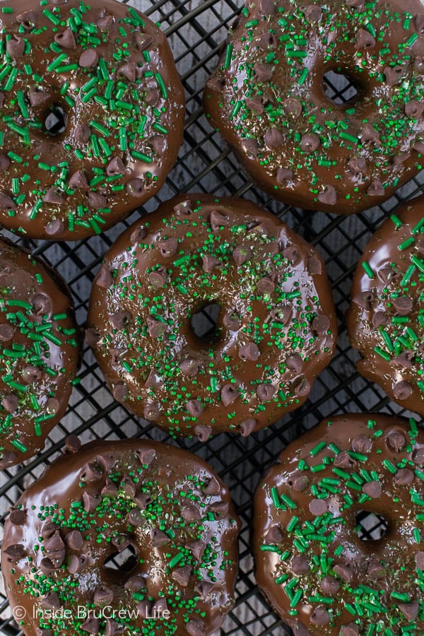 Overhead picture of glazed chocolate donuts topped with green sprinkles on a wire rack.