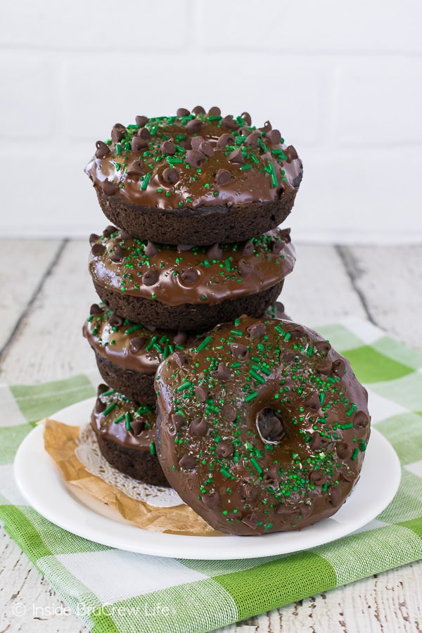 A stack of four chocolate zucchini donuts on a white plate with another donut leaning against them.