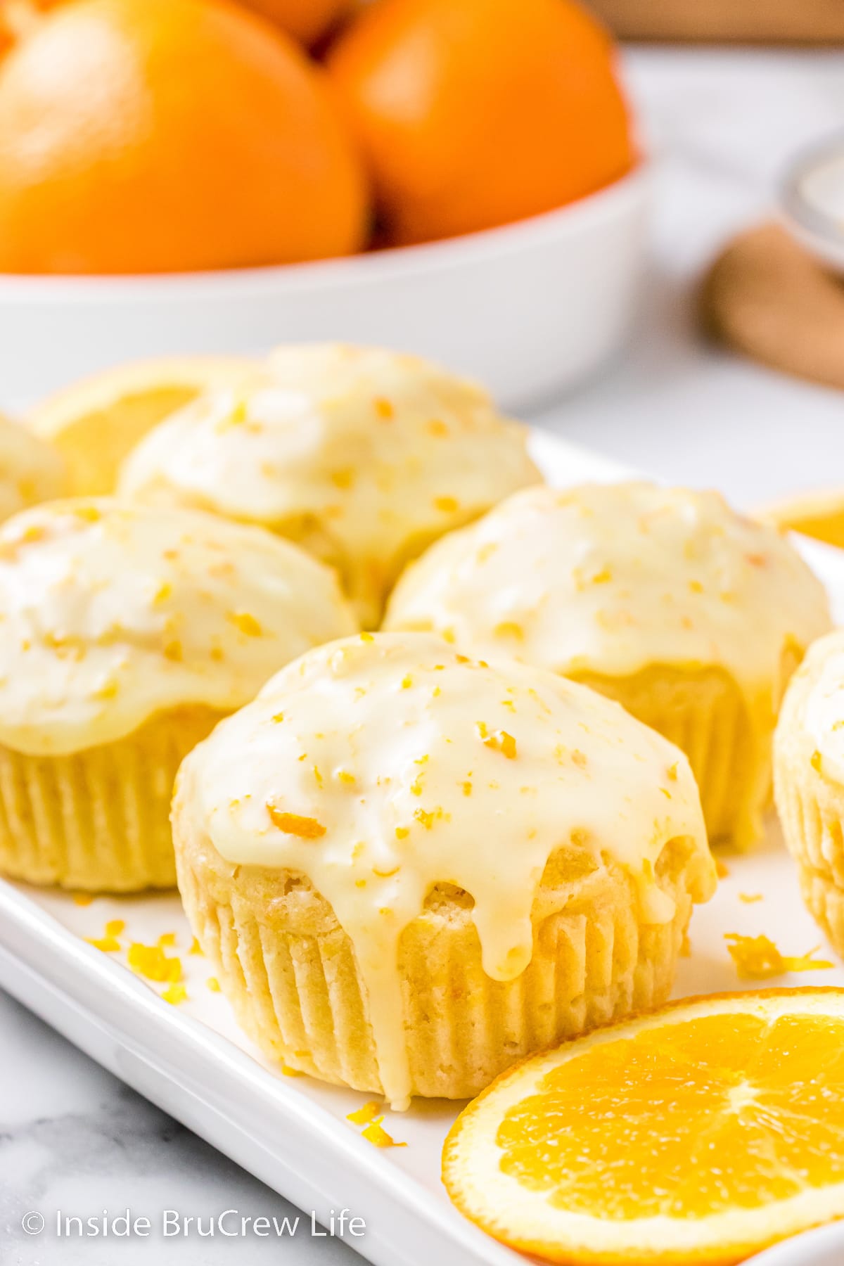 A white tray with glazed orange muffins sitting on it.