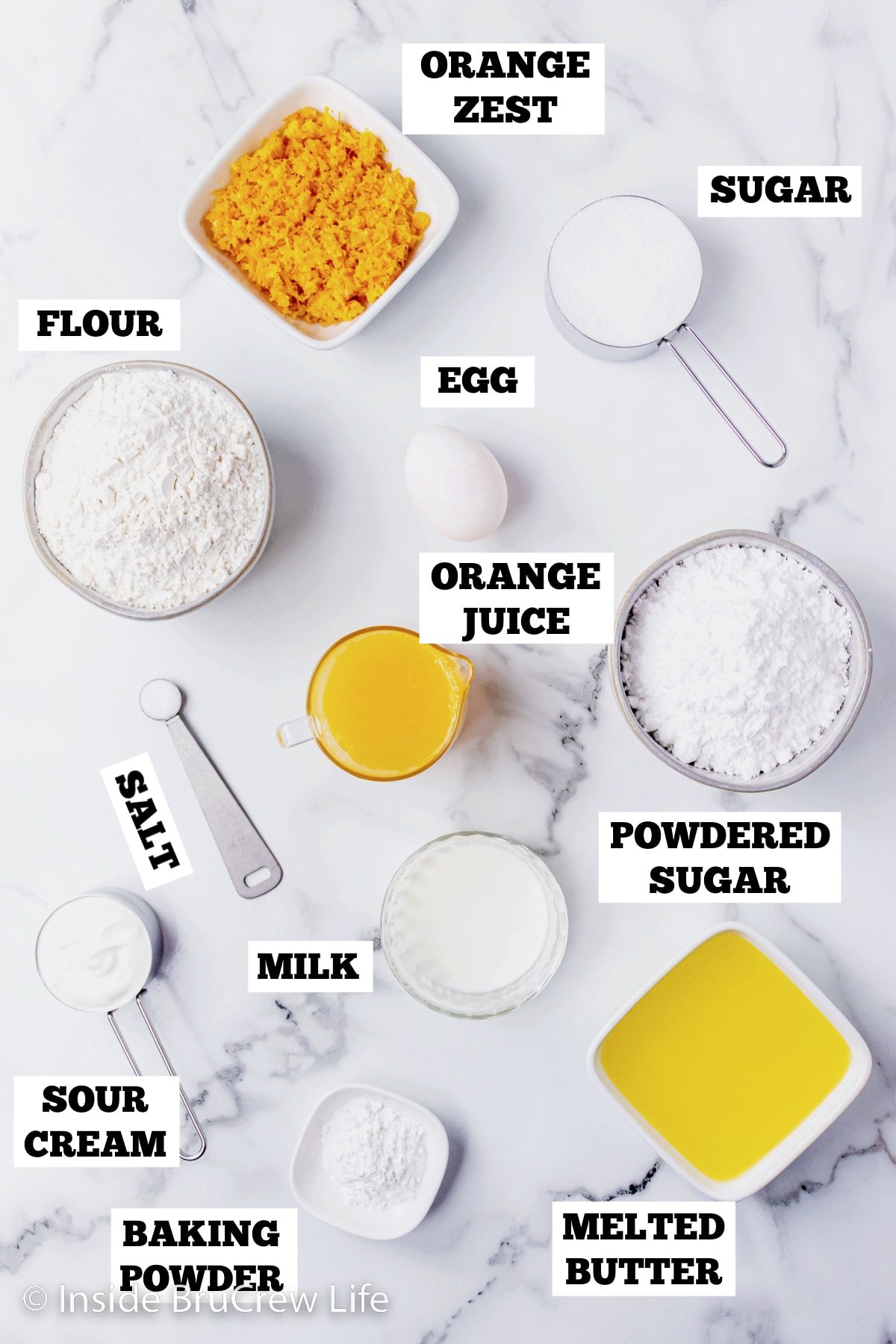 A white board with bowls of ingredients needed to make orange muffins.