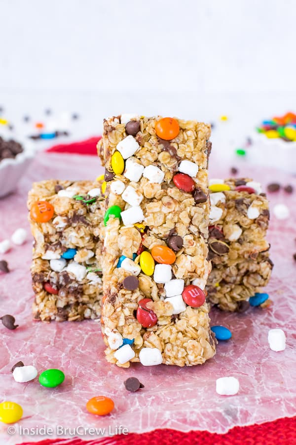No Bake M&M Granola Bars - these homemade granola bars are filled with mini M&M candies, marshmallows, and chocolate chips. Easy recipe to make for breakfast or snacks. Two granola bars on wax paper with another standing up straight against them.