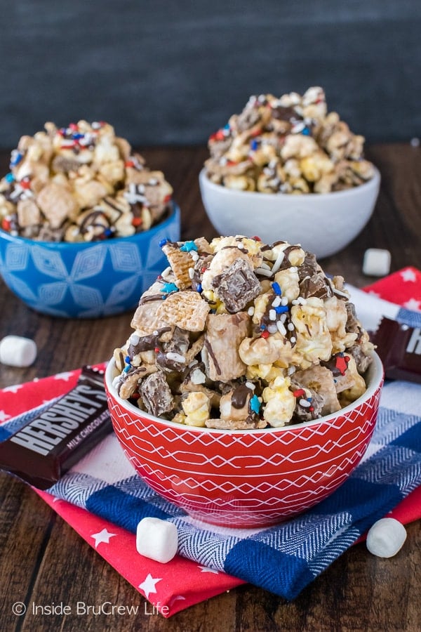 A red bowl in front with S'mores Popcorn in it and blue and white bowls behind it with more popcorn