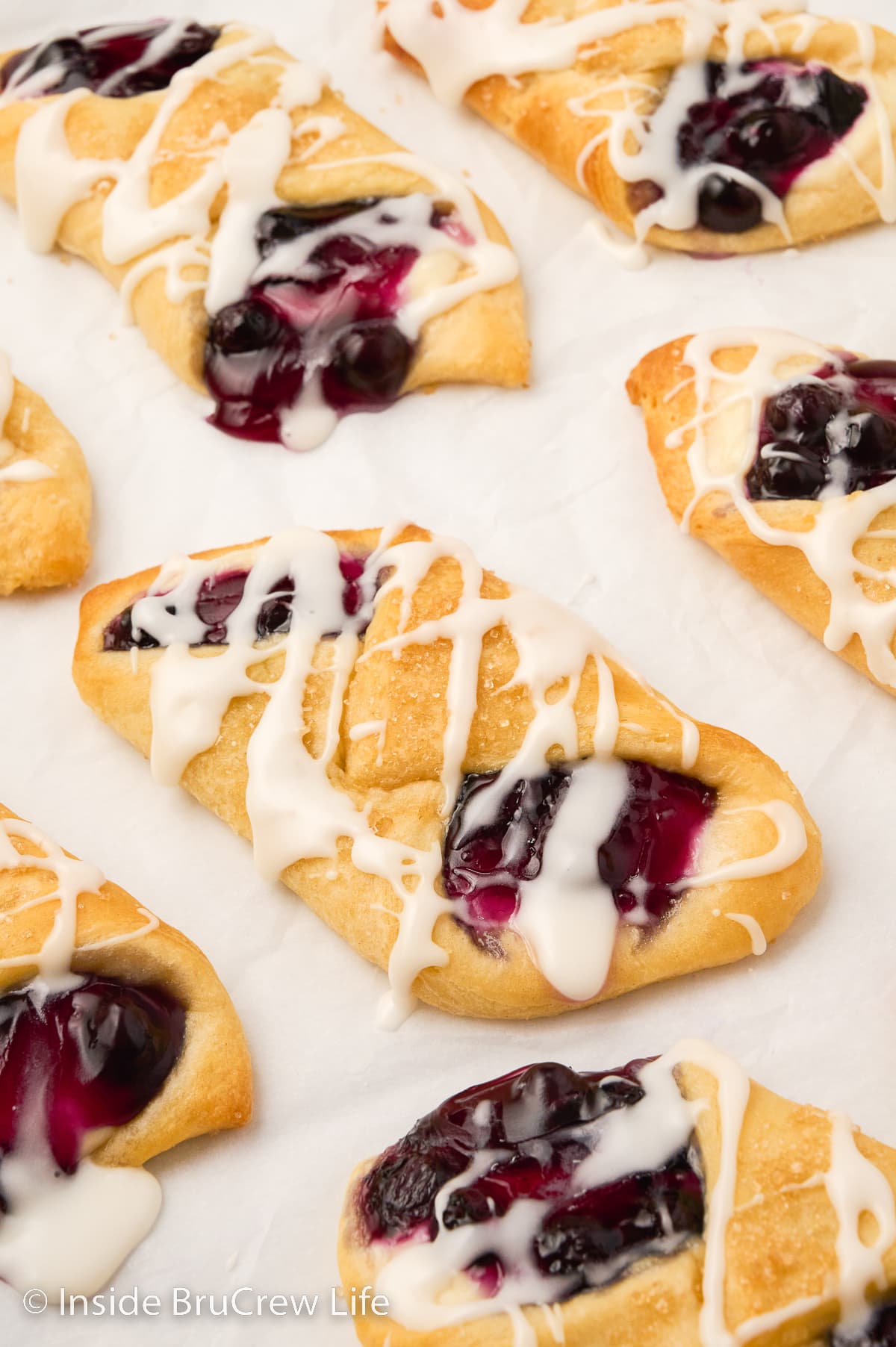 A white paper with glazed blueberry cheesecake danishes on it.