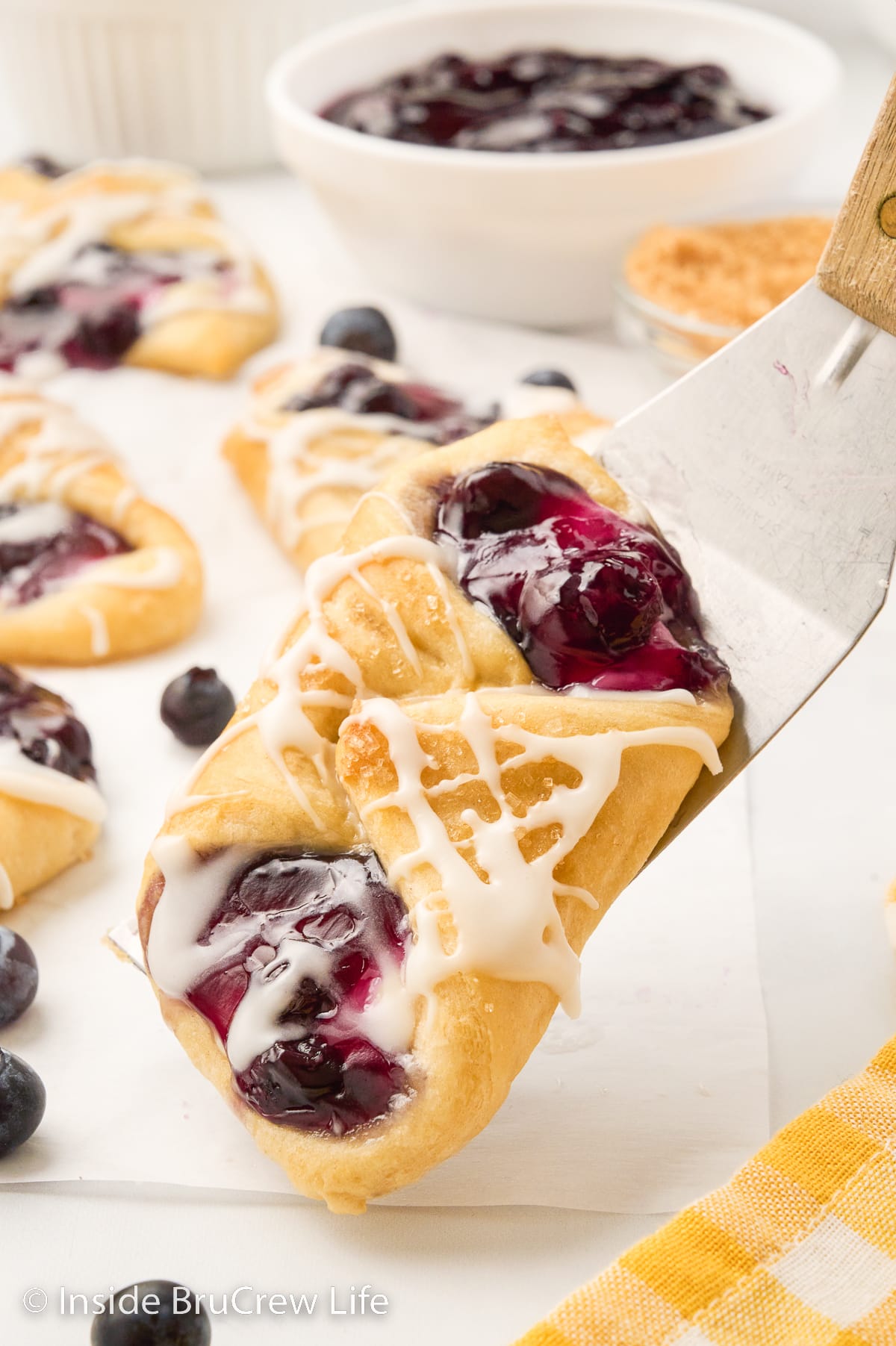 A spatula lifting a blueberry danish off parchment paper.