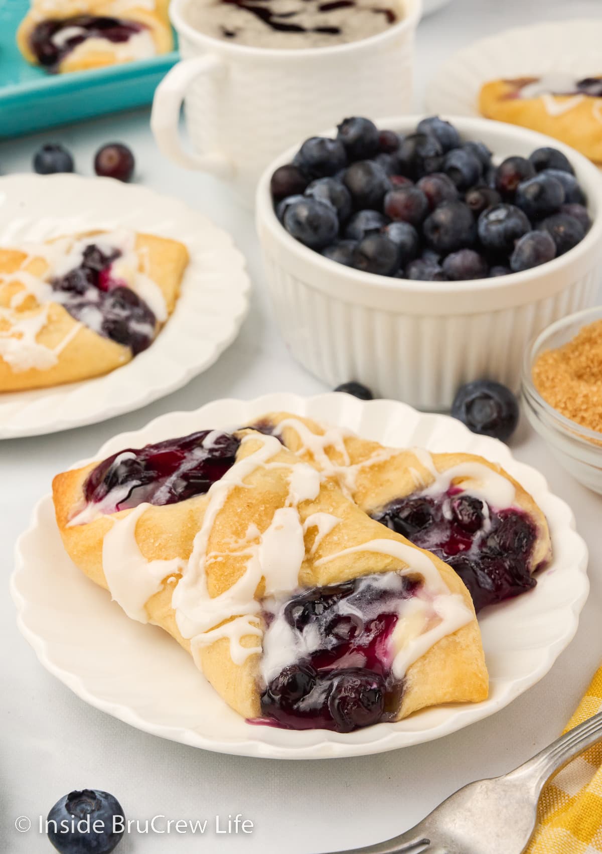 A white plate with two blueberry cheese danishes sitting on it.