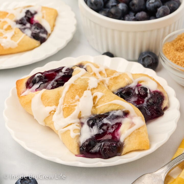 A white plate with two blueberry cheese danishes sitting on it.