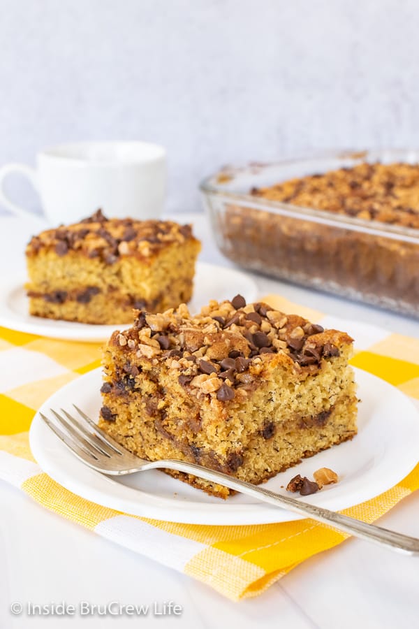 Two slices of banana toffee cake on white plates with a pan of banana cake behind them