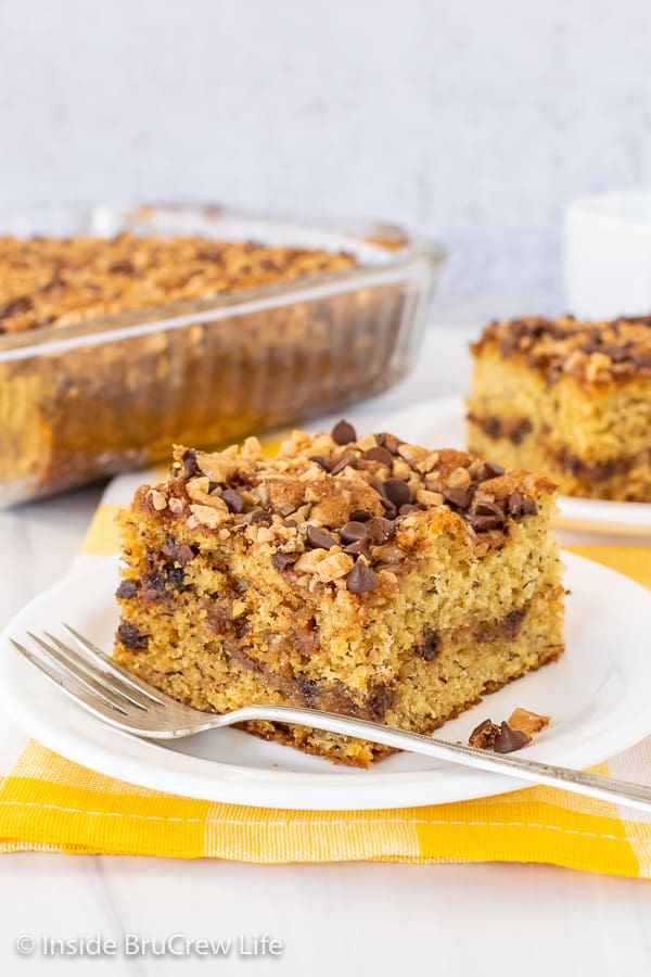 Two squares of banana toffee cake on white plates with a yellow and white dish towel under them