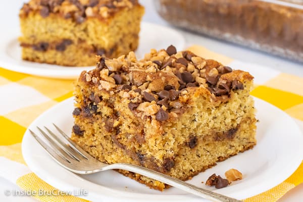 Close up picture of a square of banana toffee cake on a white plate with a fork beside it