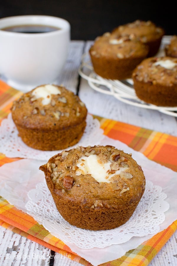 A white paper on an orange towel with two carrot cheesecake muffins on it and a tray of muffins behind it.