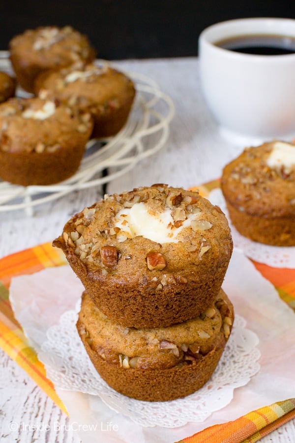 A white paper on an orange towel with two carrot cake muffins with a cream cheese center stacked on top of each other.