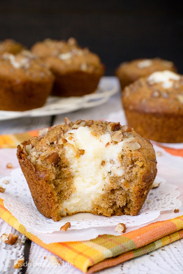 A carrot cake muffin with a cream cheese center on an orange towel with a bite taken out of it showing the cheesecake center.