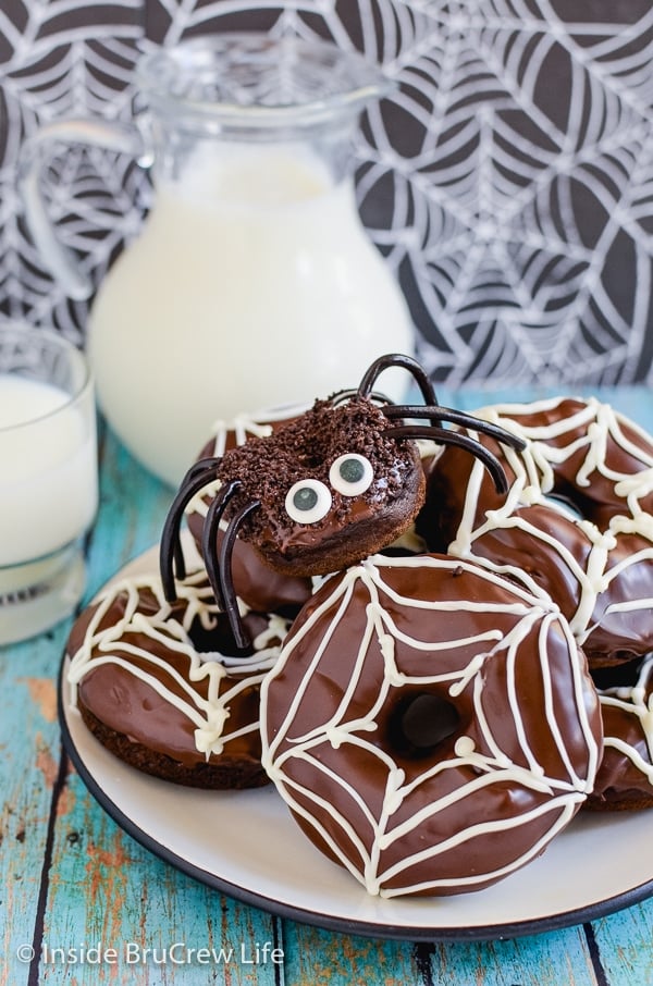 A white plate with chocolate pumpkin donuts decorated like spiders and spiderwebs piled on it