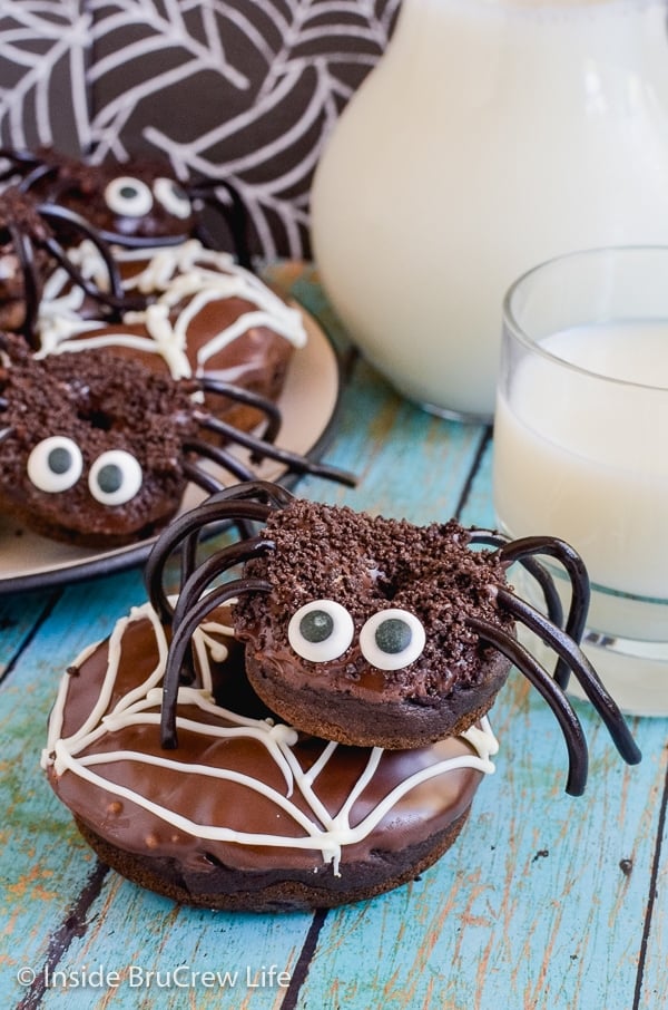 A chocolate donut decorated with a white chocolate spider web with a mini chocolate spider donut on top of it